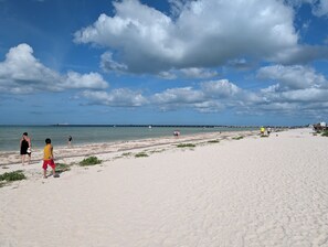 Una playa con gente caminando, un muelle a lo lejos y un cielo despejado.