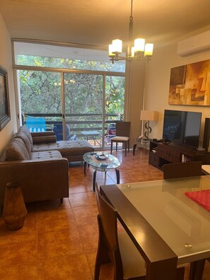 Una sala de estar moderna con un sofá, una mesa de centro de vidrio, un televisor y una mesa de comedor.