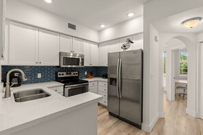 Una cocina moderna con armarios blancos, un refrigerador de acero inoxidable, un microondas y un lavamanos.