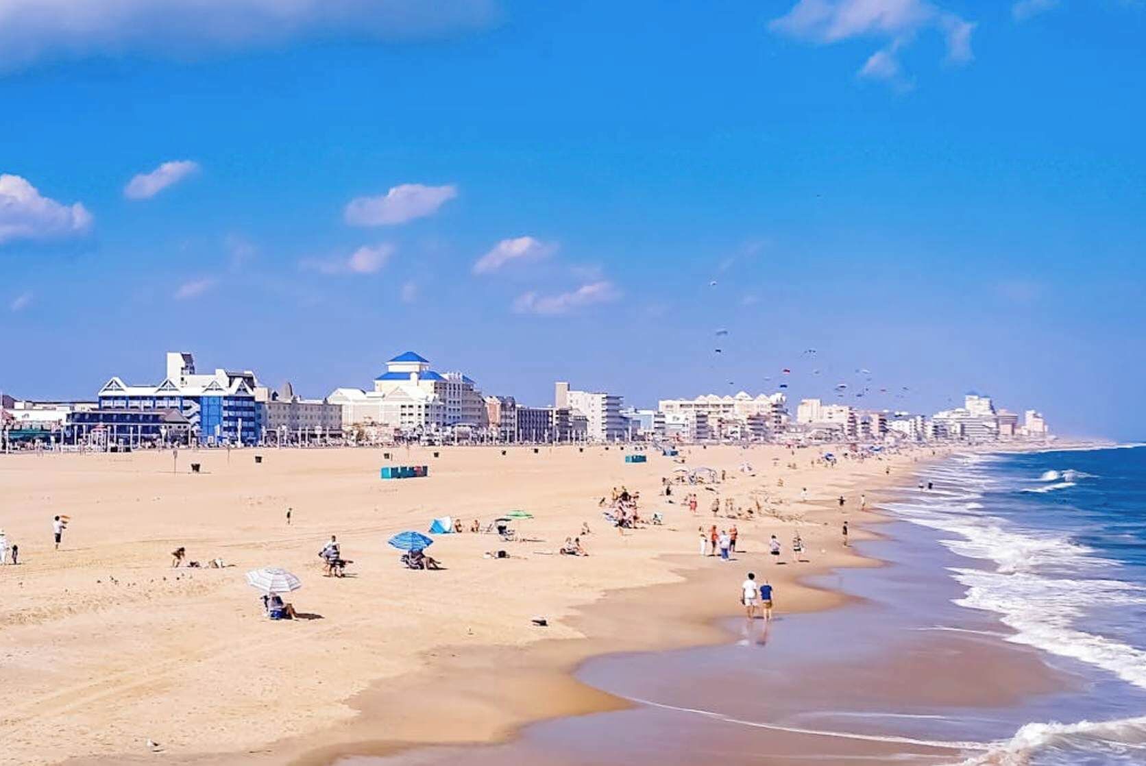 A beach with buildings in the background, people on the sand, and a clear sky.