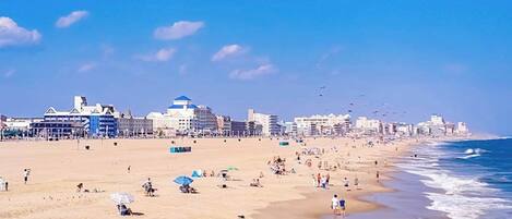 A beach with buildings in the background, people on the sand, and a clear sky.