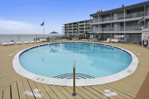 Ein Pool auf einer Terrasse mit Liegestühlen und einem Gebäude im Hintergrund.