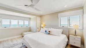 Ein Schlafzimmer mit Bett, Nachttischen, Deckenventilator und großen Fenstern mit Blick.