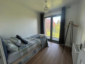 Ein kleines Schlafzimmer mit Bett, Heizkörper, einem Fenster mit Vorhängen und einer Pendelleuchte.