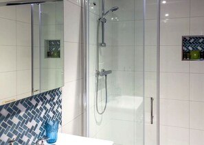 A modern bathroom with a glass-enclosed shower, white tiled walls, and a blue patterned tile backsplash.
