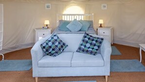 A tented room with a bed, two bedside tables with lamps, a sofa, and a window. - Yurt with Private Hot Tub and Bathroom (Bridport)