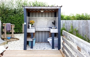 Une petite cuisine extérieure dotée d’une terrasse en bois, d’un évier et d’un espace barbecue intégré.