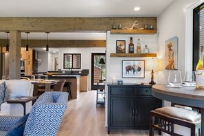 A modern kitchen with wooden beams, a dining area with a sofa, and a bar area with glasses and bottles. - Outpost: Teton Shadows Wister H - Teton Views! (Jackson)