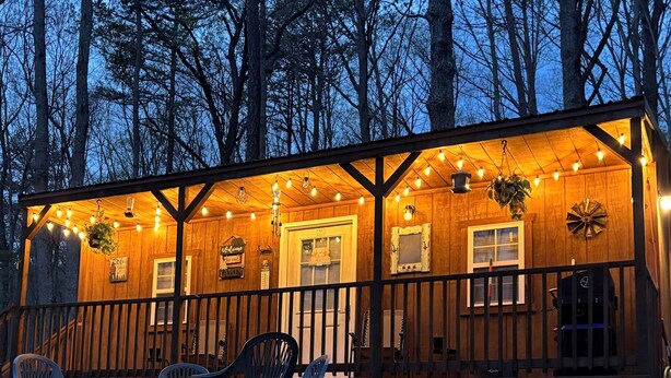 Una cabaña de madera con porche, luces colgantes y mobiliario exterior.