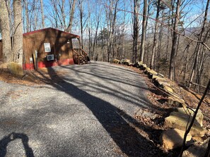 Un chemin de gravier mène à un chalet en bois avec un toit rouge, entouré d’arbres.