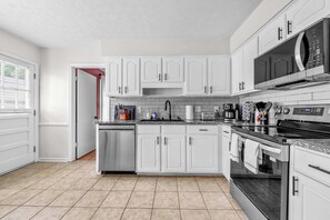 Una cucina moderna con mobili bianchi, elettrodomestici in acciaio inossidabile e backsplash piastrellato.