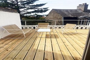 En træterrasse med hvide metalstole og et lille bord.