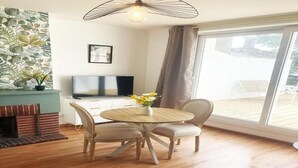 Una habitación con suelo de madera, una mesa redonda con sillas, televisor, chimenea y un ventanal grande.