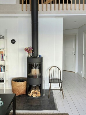 A modern living room with a black wood-burning stove, a bookshelf, a chair, and a woven basket. - Bright house with sea view at Lindö (Listerby)