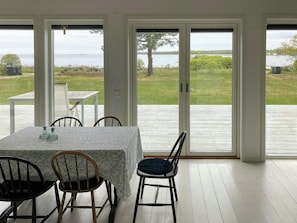 A dining area with a table and chairs, large sliding glass doors leading to a deck with a view of a lake and greenery. - Bright house with sea view at Lindö (Listerby)