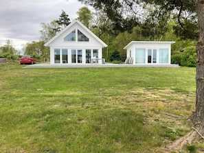 A modern two-story house with large windows, a red car parked in the driveway, and a grassy lawn. - Bright house with sea view at Lindö (Listerby)