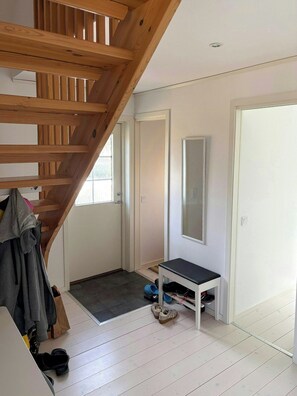 Ein Zimmer mit einer Holztreppe, einer Tür, einem Spiegel, einem kleinen Tisch und einem Schuhregal.