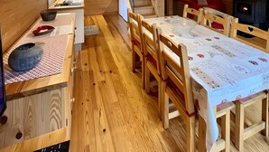 A wooden interior with a dining table, chairs, a staircase, a kitchen area, and a fireplace.