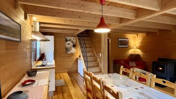 Un intérieur en bois comprenant une table à manger, des chaises, un escalier, un coin cuisine et une cheminée.