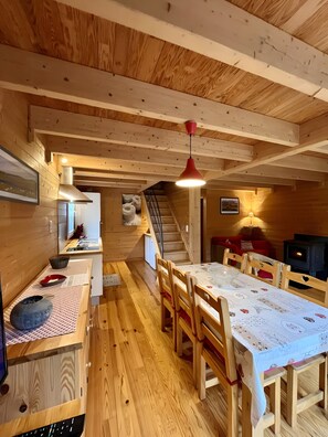 Un intérieur en bois comprenant une table à manger, des chaises, un escalier, un coin cuisine et une cheminée.