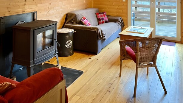 A cozy cabin interior with a wooden interior, a sofa, a table, a chair, and a wood-burning stove.