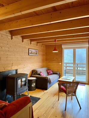 L’intérieur chaleureux d’un chalet, avec un décor en bois, un canapé, une table, une chaise et un poêle à bois.