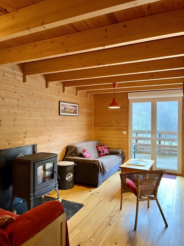 L’intérieur chaleureux d’un chalet, avec un décor en bois, un canapé, une table, une chaise et un poêle à bois.