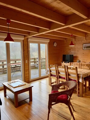 Un intérieur en bois avec un coin repas, de grandes fenêtres et une horloge au mur.
