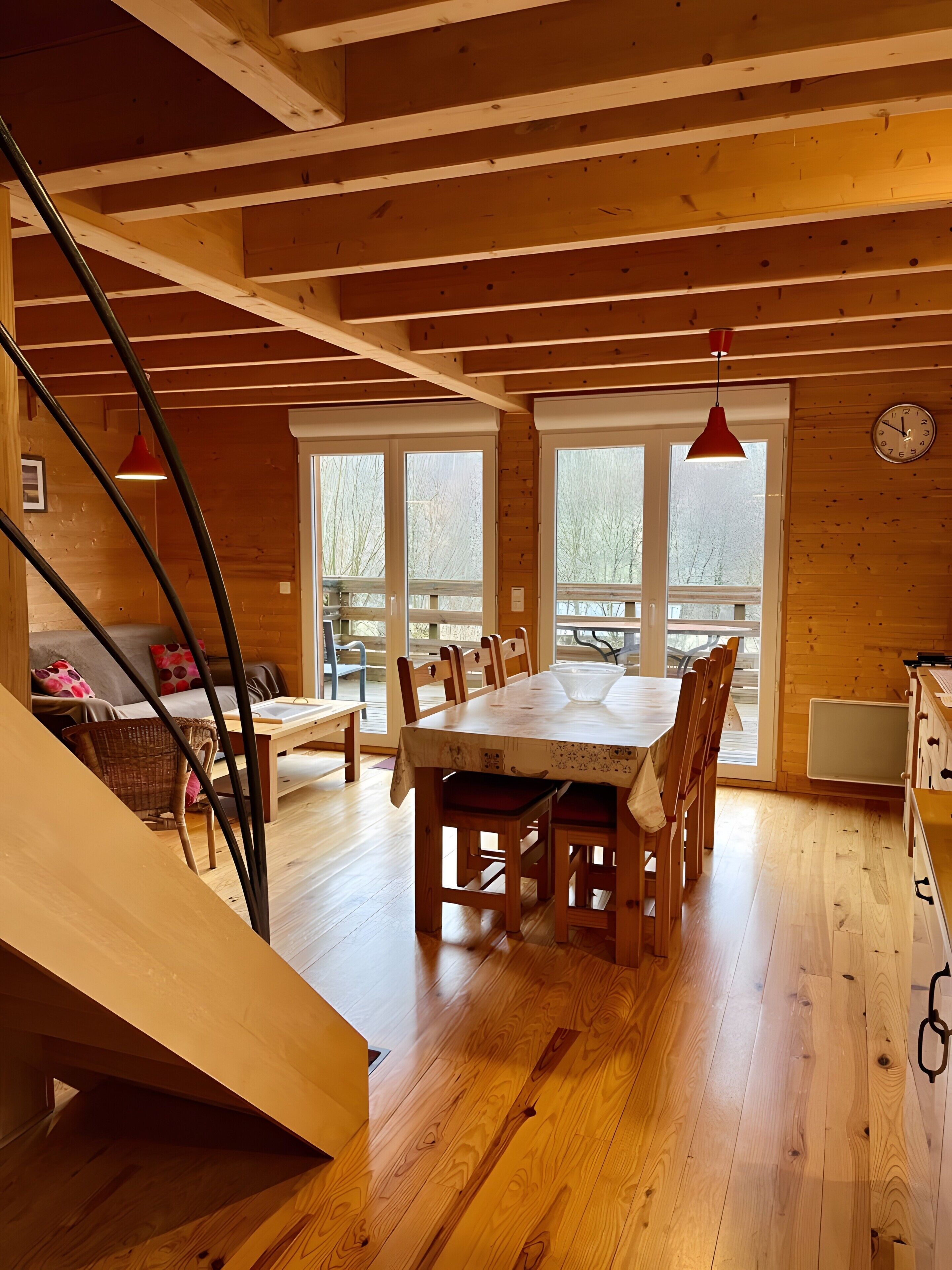 Un interior de madera con una mesa de comedor, sillas, una escalera y vistas amplias a través de grandes ventanales.