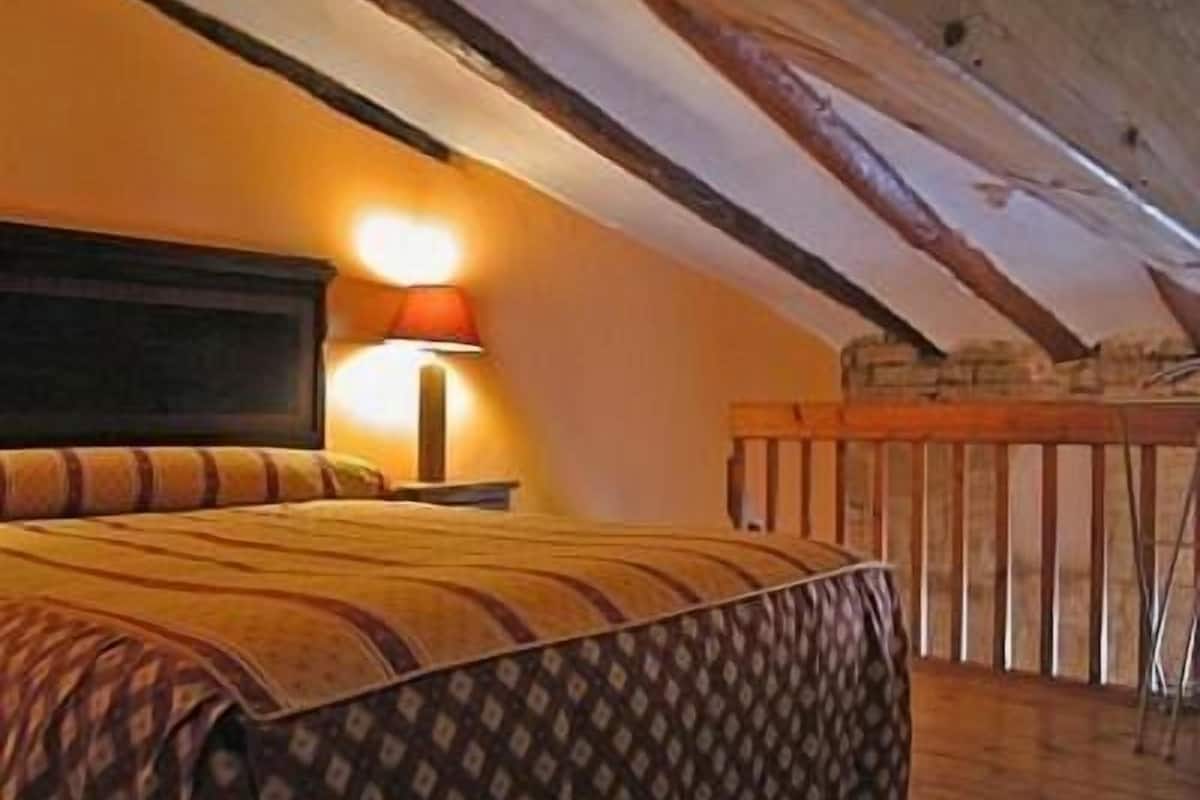 A bedroom with a bed, a nightstand, a lamp, and a balcony with a railing.
