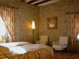 Una habitación con paredes de piedra, una cama con cubrecama floral, dos sillas, una lámpara de pie y un cuadro en la pared.