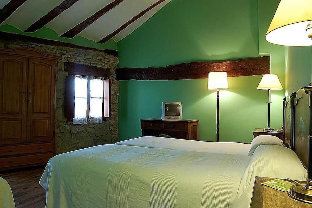 A bedroom with a bed, a stone wall, wooden wardrobe, and two lamps.