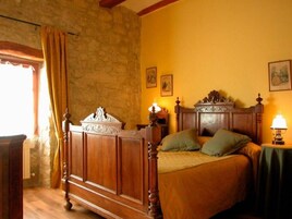 Un dormitorio con cama de madera, pared de piedra y ventana con cortinas.
