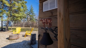 A wooden cabin with a bell and a cow decoration on the wall, a chair, and a fire pit in the yard. - Lakeview Escape at Gimli by Guest Expertise (gimli)