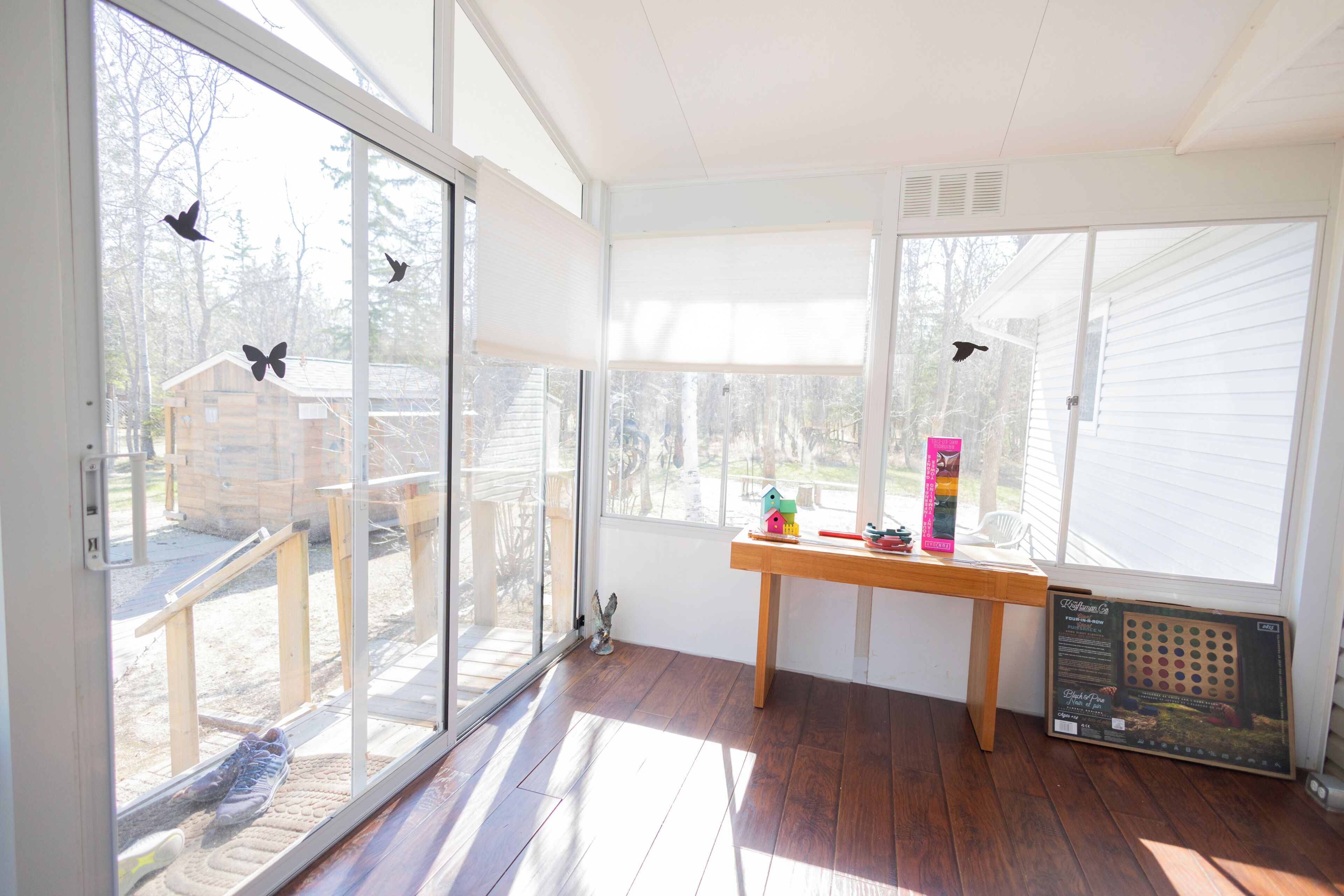 Ein Zimmer mit großen Fenstern, einem Holztisch und Blick auf eine Holzterrasse und ein Haus.