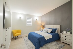 Une chambre à coucher avec un lit, des tables de chevet, une chaise, un téléviseur et une fenêtre.