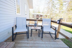 Une terrasse en bois avec deux chaises et une petite table, un chien sur la table et une pancarte indiquant « BIENVENUE ».