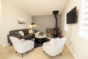 A modern living room with a sofa, two armchairs, a coffee table, a fireplace, and a television mounted on the wall.