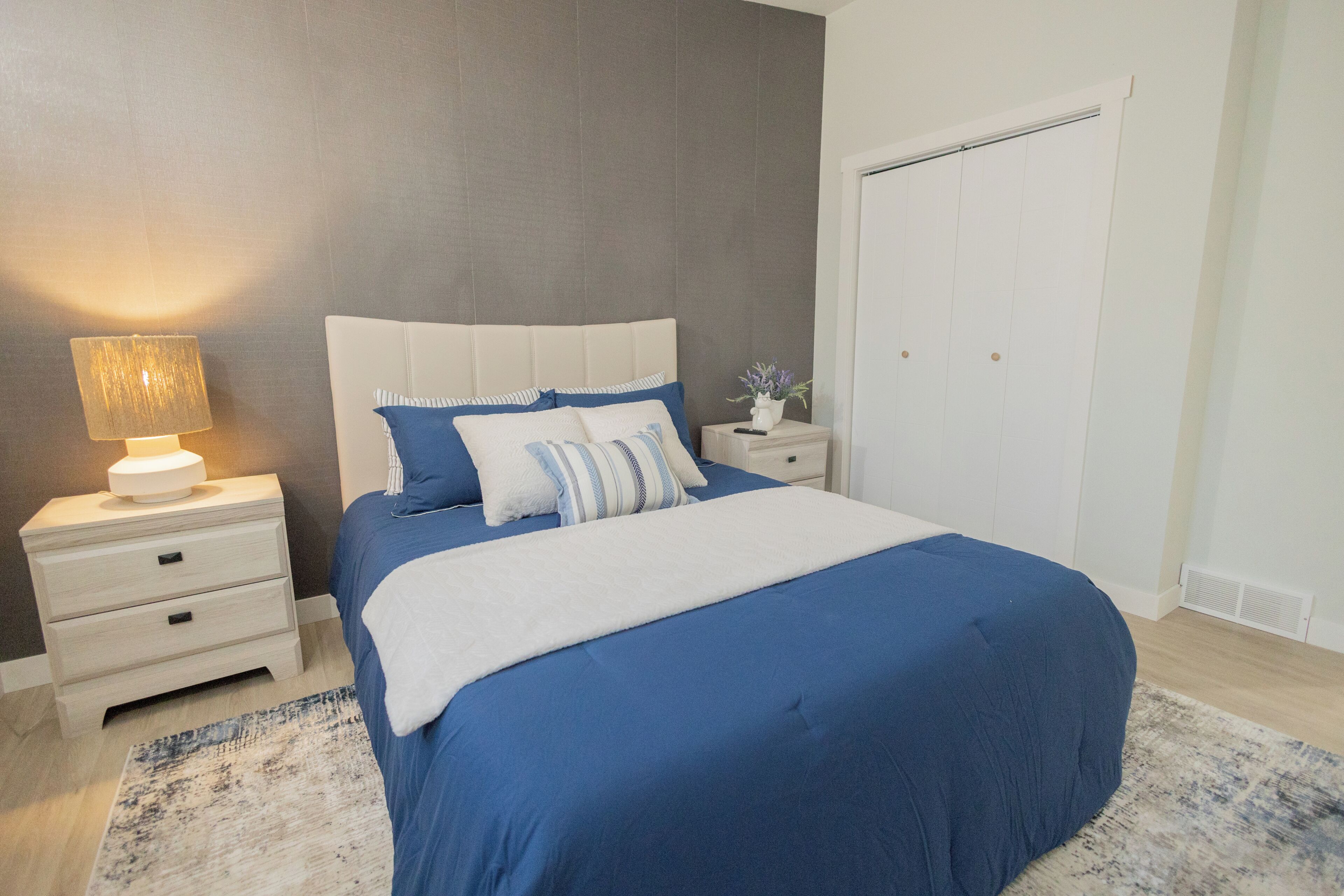 Ein Schlafzimmer mit einem Bett, Nachttischen, einer Lampe, einem Nachtschränkchen und einem Kleiderschrank.
