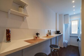 Una cocina con una encimera amplia, una cafetera, un hervidor y un cubo de basura.