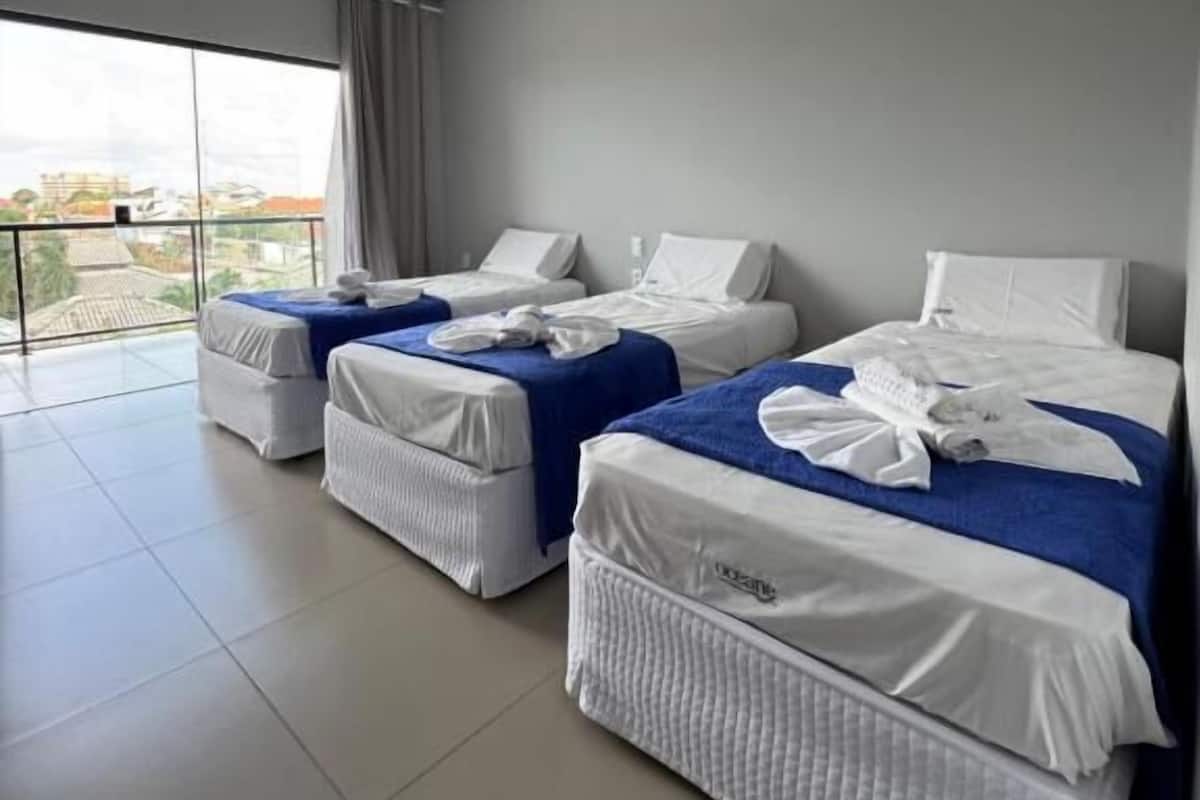 Une chambre d’hôtel avec trois lits, une grande fenêtre et un balcon.