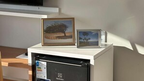 A white cabinet with two framed pictures, a black device with a label, and a wooden surface below. - Oceane Norte Hotel (Parnaíba)