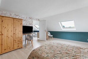 Ein Schlafzimmer mit einem Bett, einem Holzschrank, einem Schreibtisch mit Stuhl, einem Fernseher und einem Oberlicht.