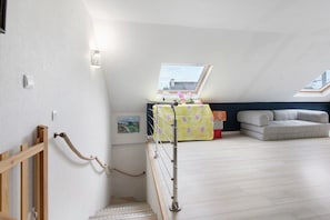 A loft bedroom with a skylight, a staircase, a sofa, and a small table with a floral tablecloth.