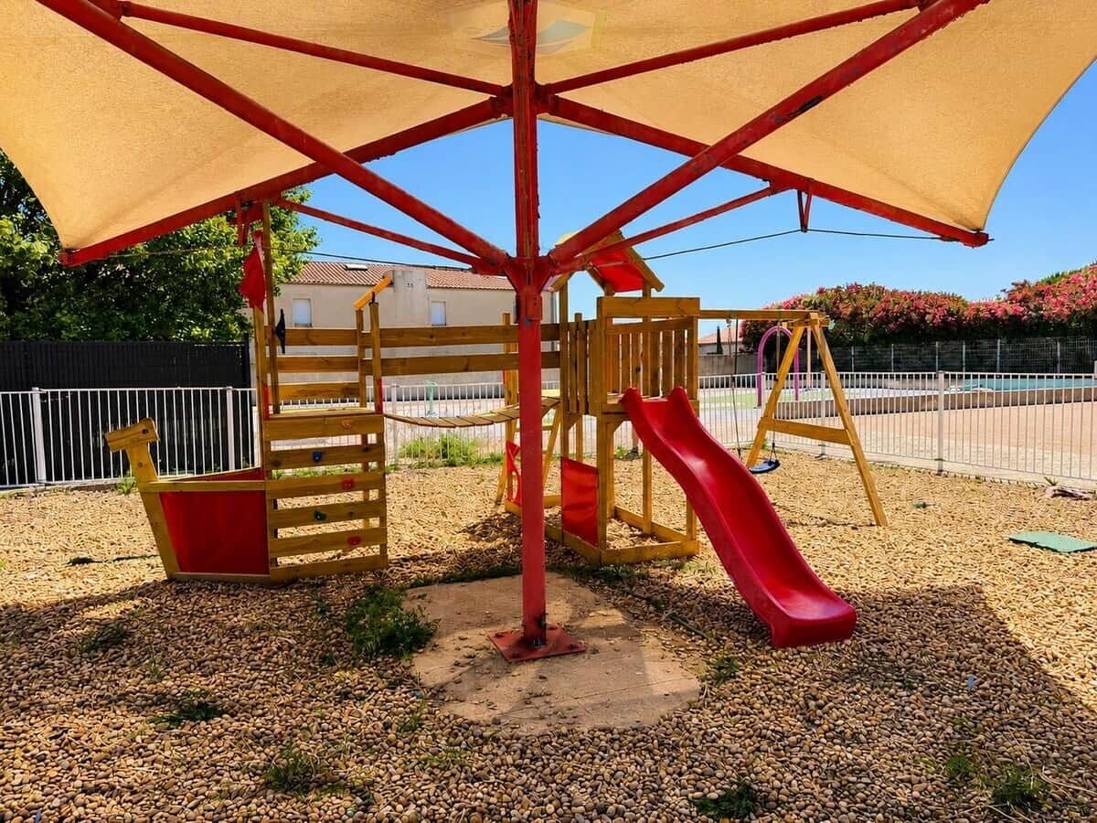 A playground with a slide, climbing structures, and a shaded area.