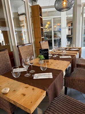 Un restaurante con mesas de madera y sillas de mimbre, un atril para el menú y lámparas colgantes.