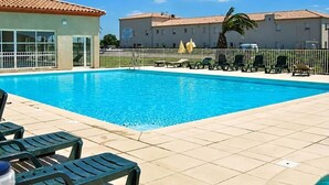 A swimming pool with lounge chairs, a building with a tiled roof, and a palm tree. - La parenthèse Camarguaise (Gallargues-le-Montueux)