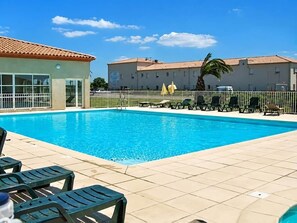 Una piscina con sillas de descanso, un edificio con techo de tejas y una palmera.