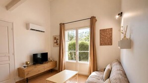 A living room with a sofa, TV, wooden cabinet, and a window with curtains. - La parenthèse Camarguaise (Gallargues-le-Montueux)