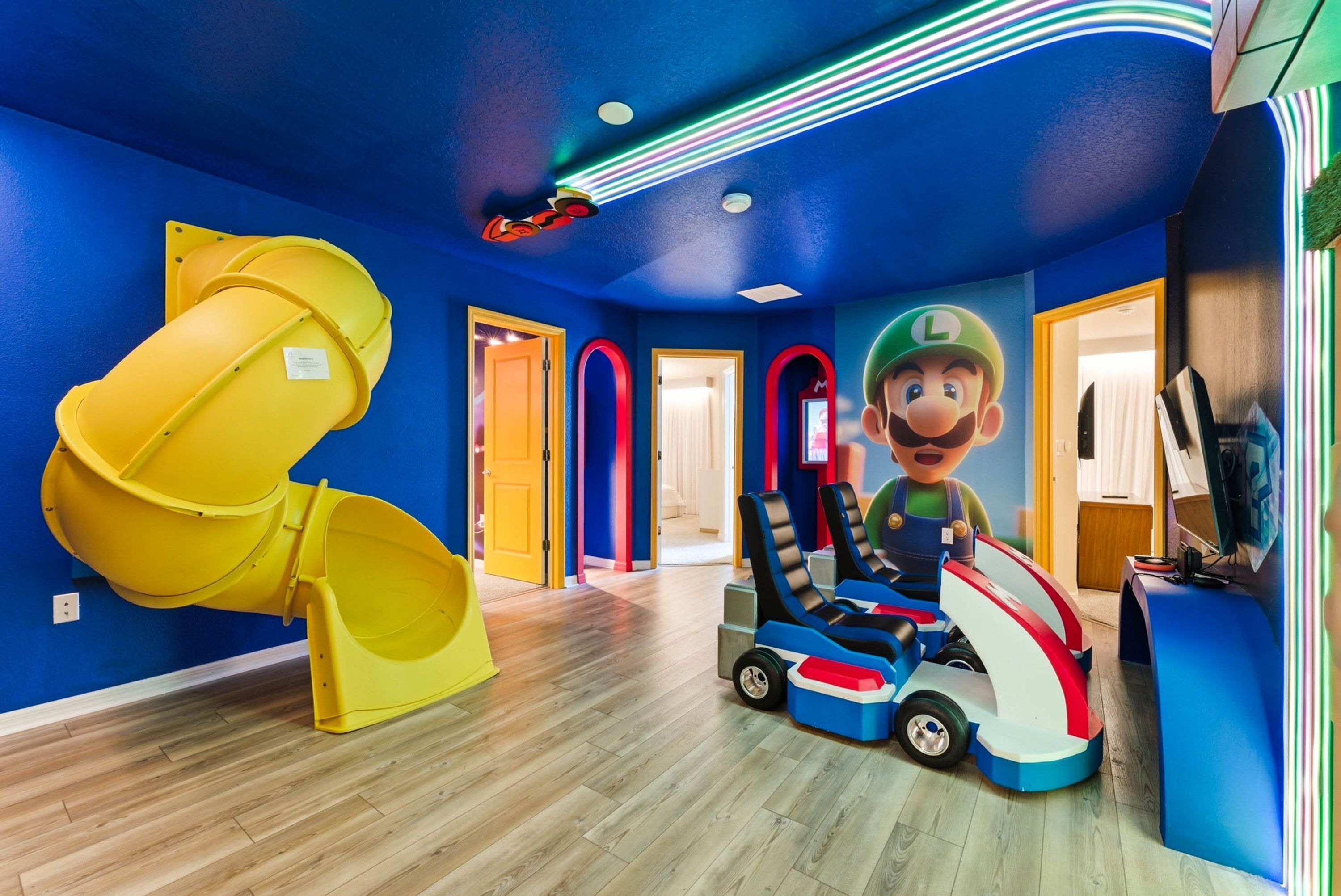 Ein Spielbereich mit einer gelben Rutsche, einem Mario-Spielzeugauto und einem großen Mario-Wandbild.